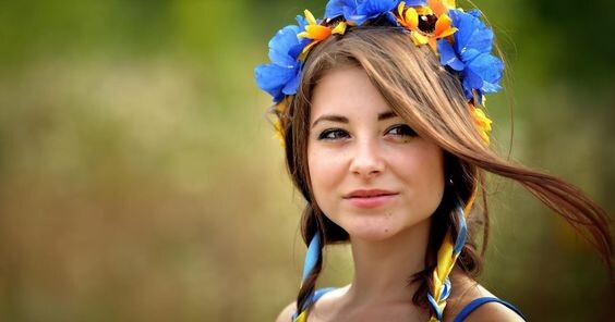 Zdjęcie przedstawia lekko uśmiechniętą kobietę z niebiesko-żółtym wiankiem na głowie.